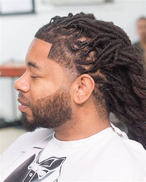 These long dreadlocks are gathered in a low man bun, with the highlighted section of hair loosely tied and pinned back. . Dreads with front taper